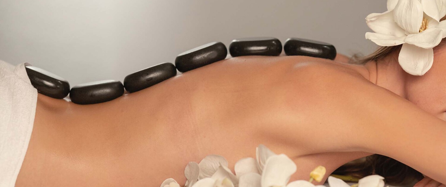 Massaggio Hot Stone con pietre laviche calde posizionate lungo la colonna vertebrale presso ConTatto Wellness Massage a Varese. Trattamento decontratturante e riequilibrante per corpo e mente